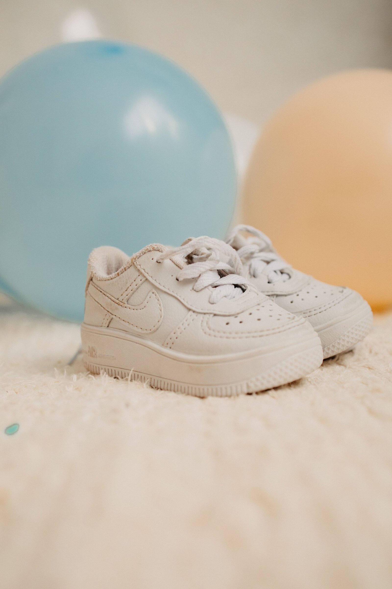 Cute white baby sneakers with pastel balloons in the background, perfect for baby-themed content.